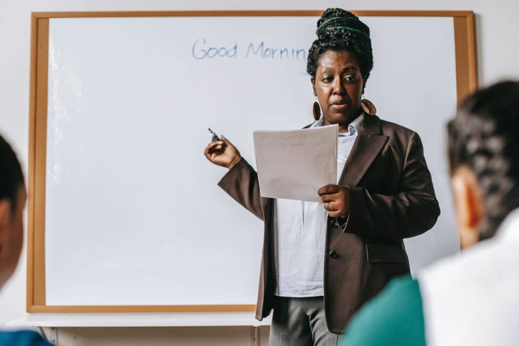 A Black person stands in front of a white board with the words "Good Morning" written in blue marker
